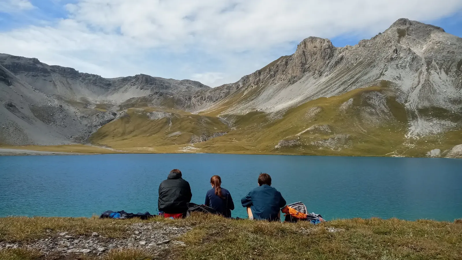 Drei Personen sitzen an einem Bergsee